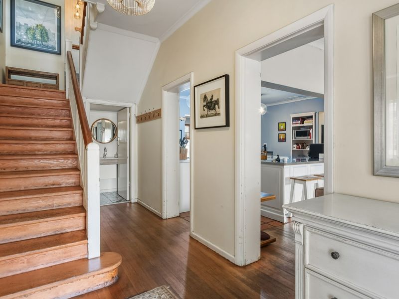 A welcoming hallway featuring polished timber flooring and a classic wooden staircase, providing access to adjacent living areas and a ground-floor washroom.
