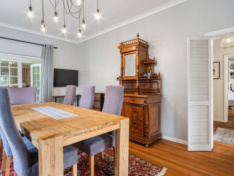 A well-maintained dining room featuring polished hardwood floors, elegant cove cornicing, and direct access to the patio through classic French doors.