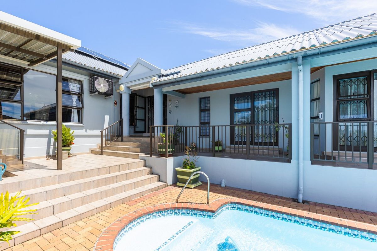 A well-maintained rear exterior featuring a tiled patio, swimming pool, and covered veranda area with metal security gates and railings.