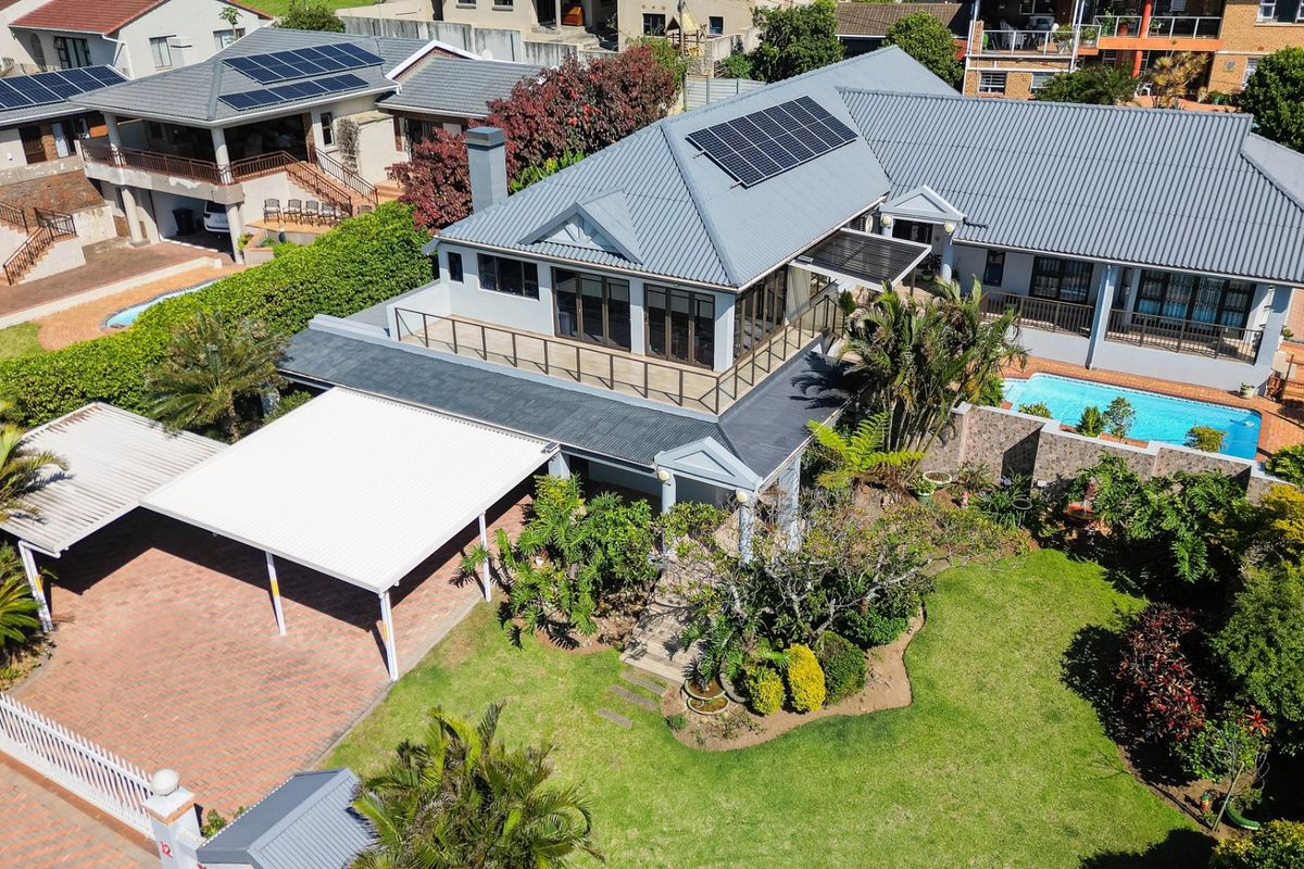 Aerial view of a residential property featuring a metal roof with solar panels, a swimming pool, a paved driveway, and a covered carport.