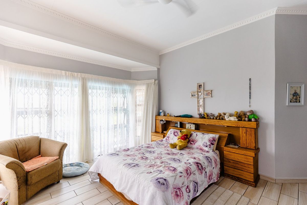 A bedroom featuring built-in wooden headboard cabinetry, tiled flooring, and large sliding glass doors with security gates leading to an outdoor area.