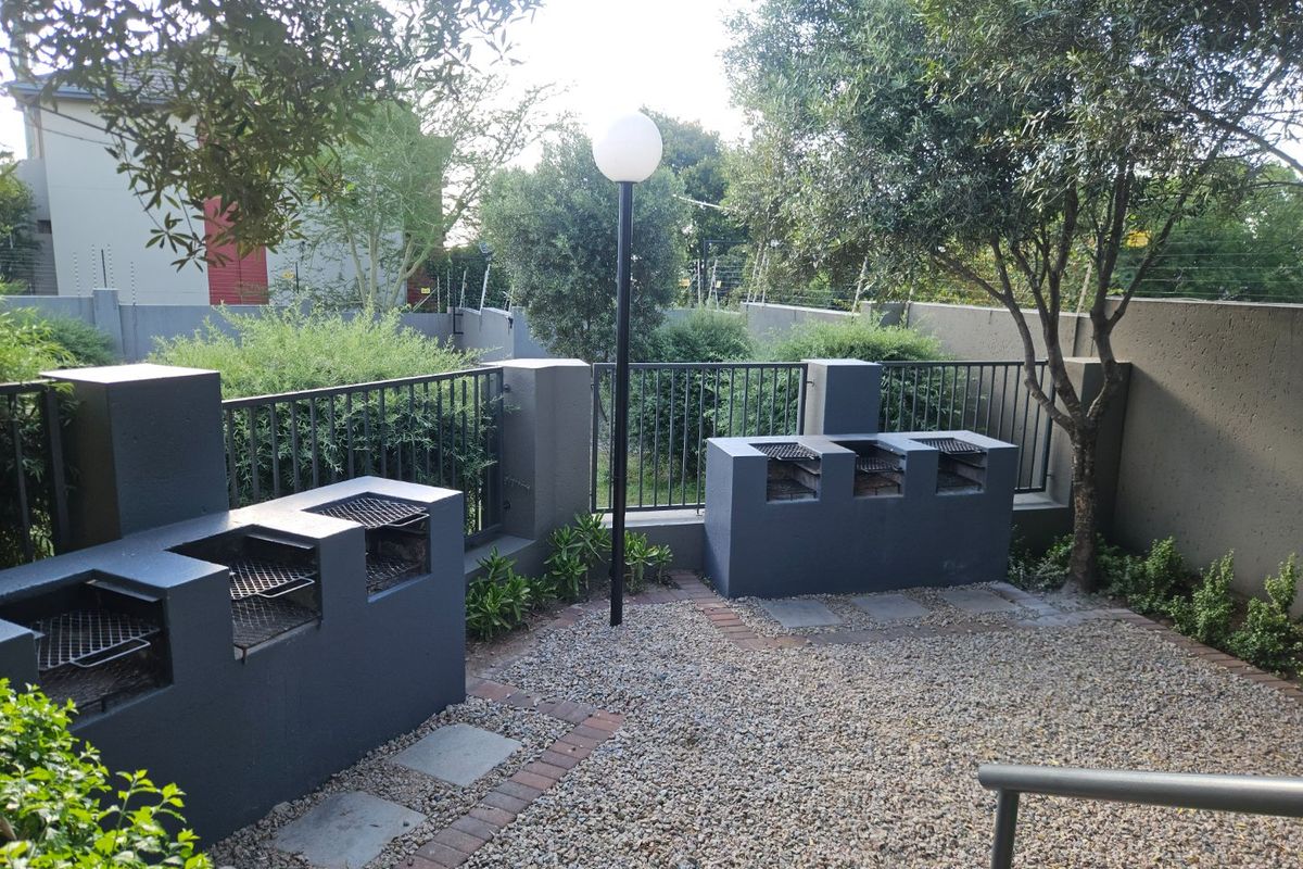 A well-maintained outdoor entertainment area featuring dual built-in braai stations, gravel flooring, and secure perimeter fencing within a landscaped garden setting.