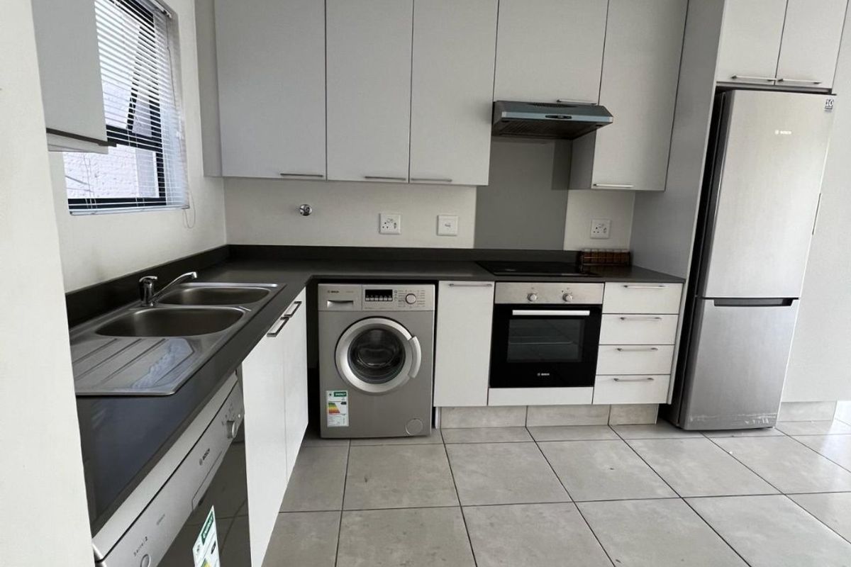 Modern kitchen featuring light grey cabinetry, stone countertops, integrated appliances, and neutral tiled flooring in a clean, functional layout.