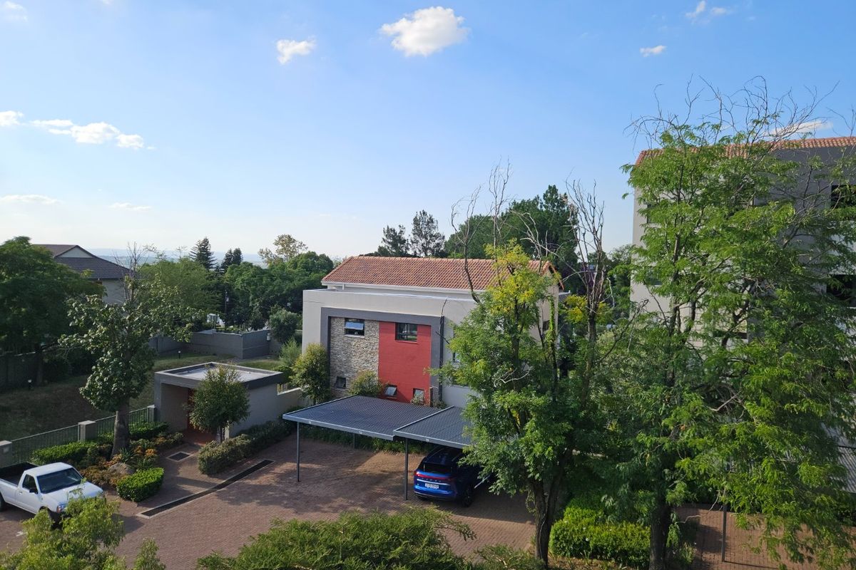 An elevated aerial view of the property complex, featuring a paved driveway, covered carport parking, and well-maintained landscaped garden areas.