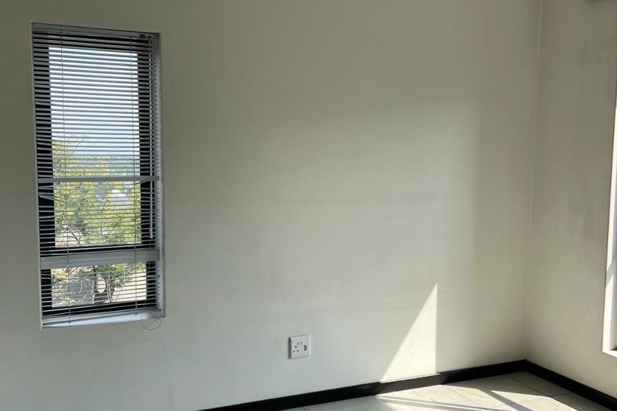 A bright, empty bedroom featuring neutral tiled flooring, clean walls, and a window fitted with venetian blinds.
