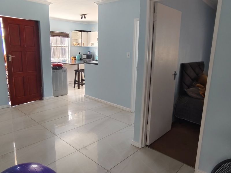 Open plan living area featuring tiled flooring, connecting to a kitchen space with built-in cabinetry and a breakfast counter.