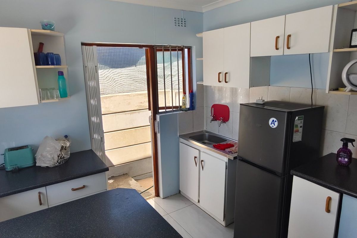 A functional kitchen featuring built-in cabinetry, laminate countertops, a stainless steel sink, and direct access to an outdoor area through a folding security door.