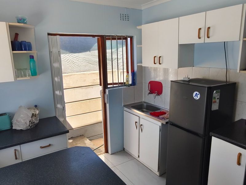 A functional kitchen featuring built-in cabinetry, laminate countertops, a stainless steel sink, and direct access to an outdoor area through a folding security door.
