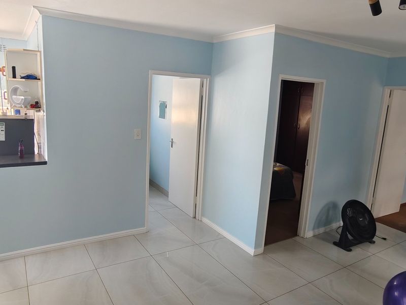 Open plan living area featuring light blue walls, tiled flooring, and access to multiple rooms and an outdoor patio area.
