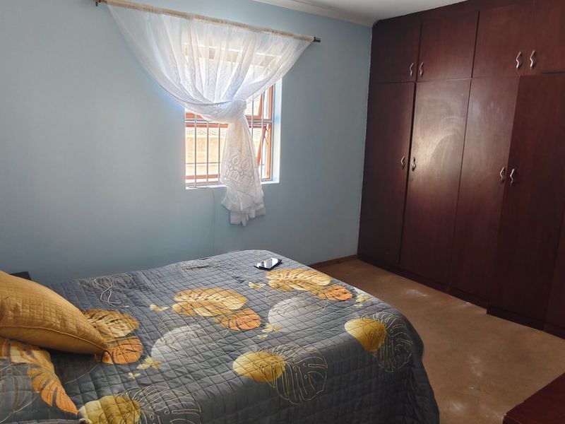 A bedroom featuring built-in wooden cupboards and a window with security bars, offering a functional space with potential for cosmetic updates.