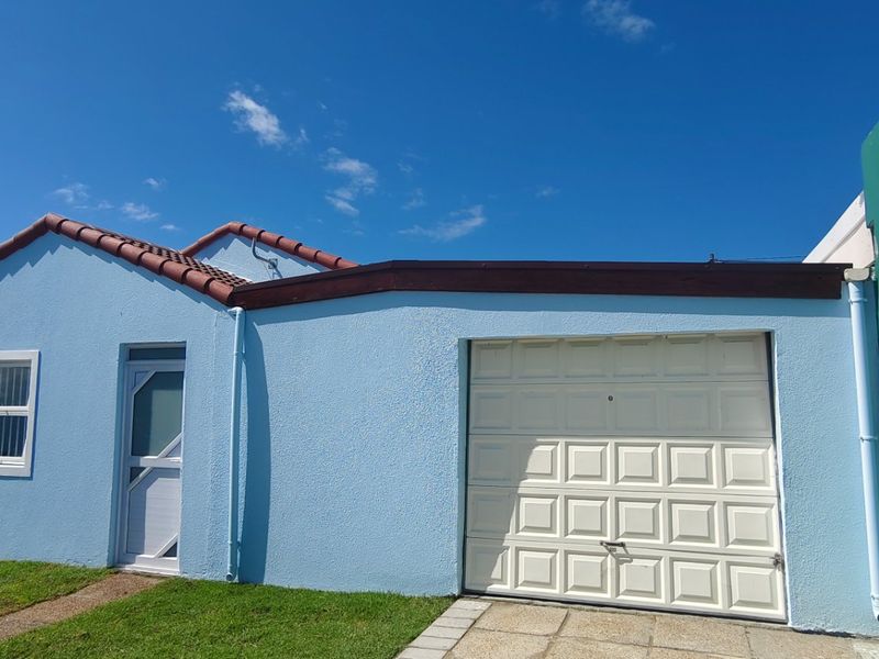 Front elevation of a single-story house featuring a light blue facade, a white garage door, and a tiled roof.