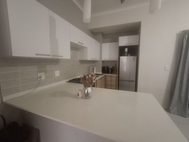 Modern kitchen featuring white cabinetry, stone countertops, a gas hob, and a tiled backsplash, offering a clean and functional cooking space.