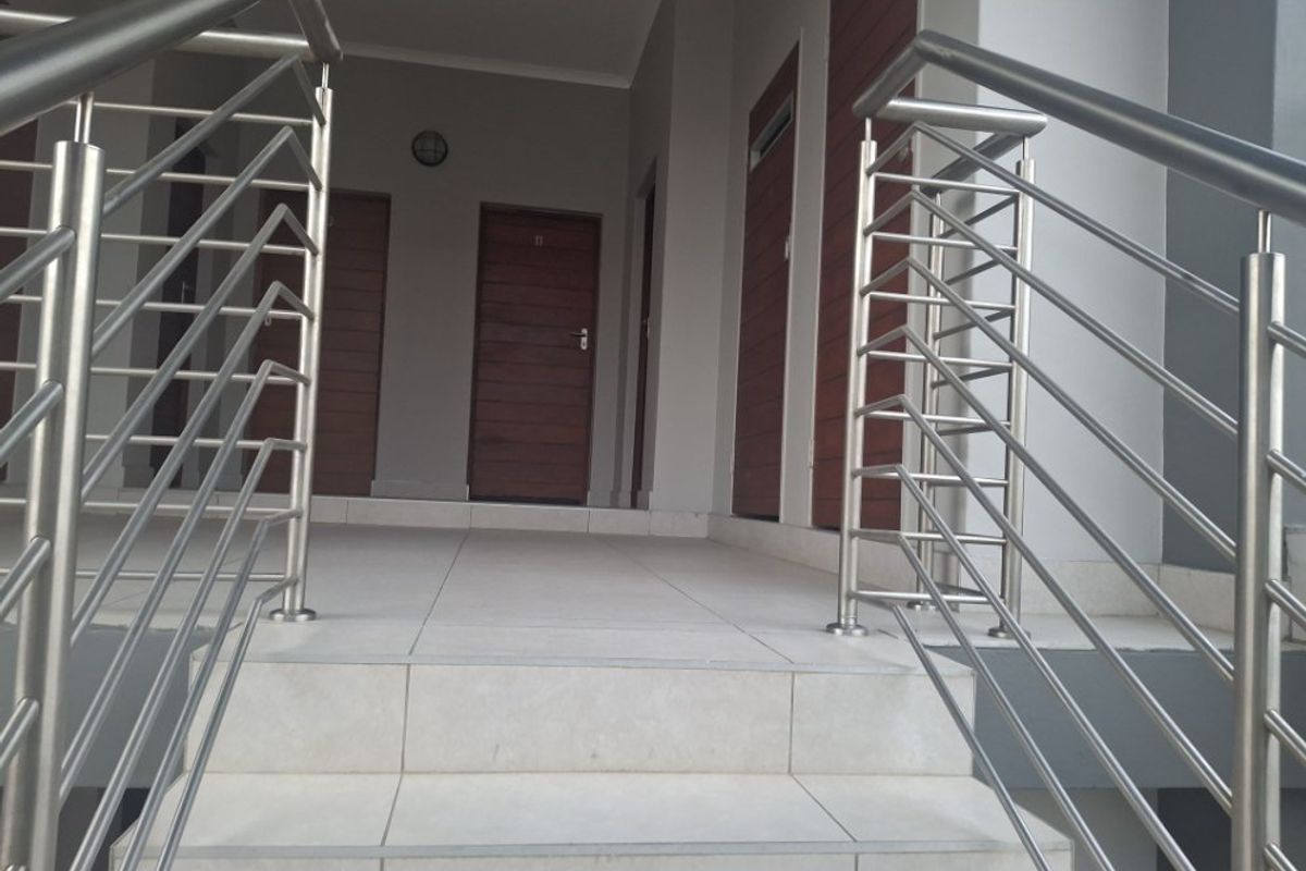Entrance area featuring a tiled staircase with modern stainless steel balustrades leading to multiple wooden apartment entry doors.