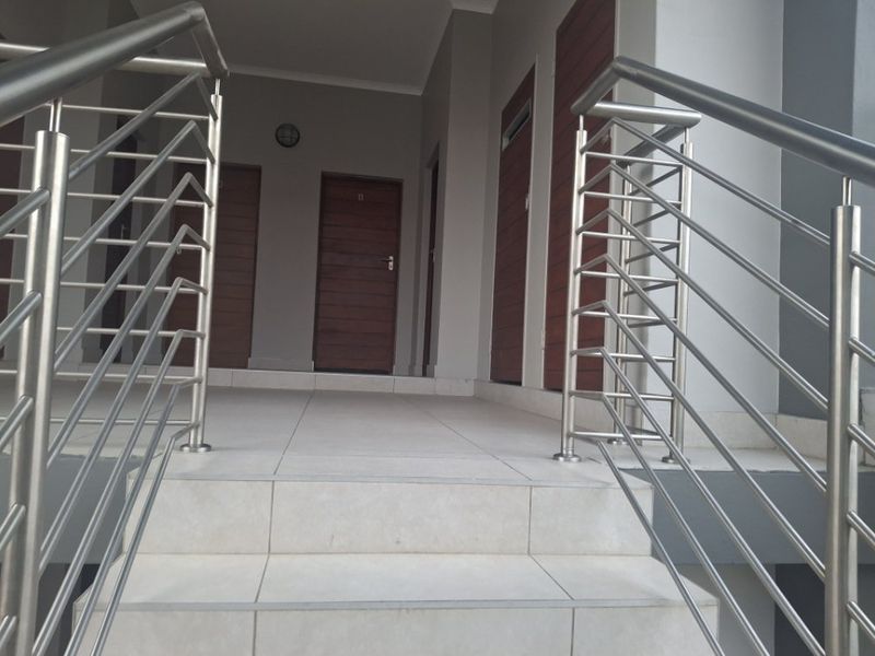 Entrance area featuring a tiled staircase with modern stainless steel balustrades leading to multiple wooden apartment entry doors.