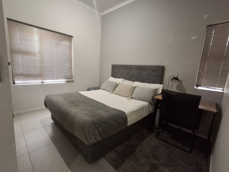 A well-maintained bedroom featuring neutral tiled flooring, clean wall finishes, and fitted venetian blinds on the windows.