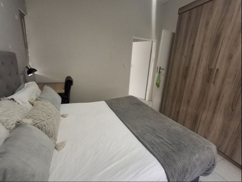 A functional bedroom featuring a large built-in wooden wardrobe and neutral wall finishes, providing a clean and practical living space.