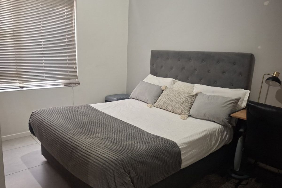 A functional bedroom featuring neutral tiled flooring and venetian blinds, providing a clean and simple space ready for personalization.