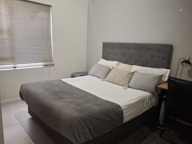 A functional bedroom featuring neutral tiled flooring and venetian blinds, providing a clean and simple space ready for personalization.