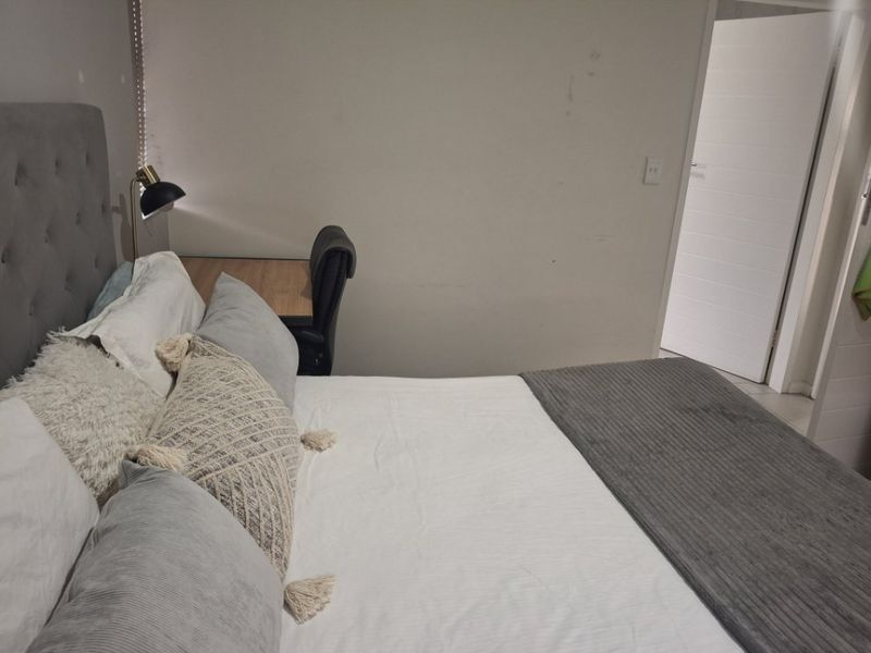 A bedroom featuring a neutral color palette with an upholstered headboard and access to an internal hallway.