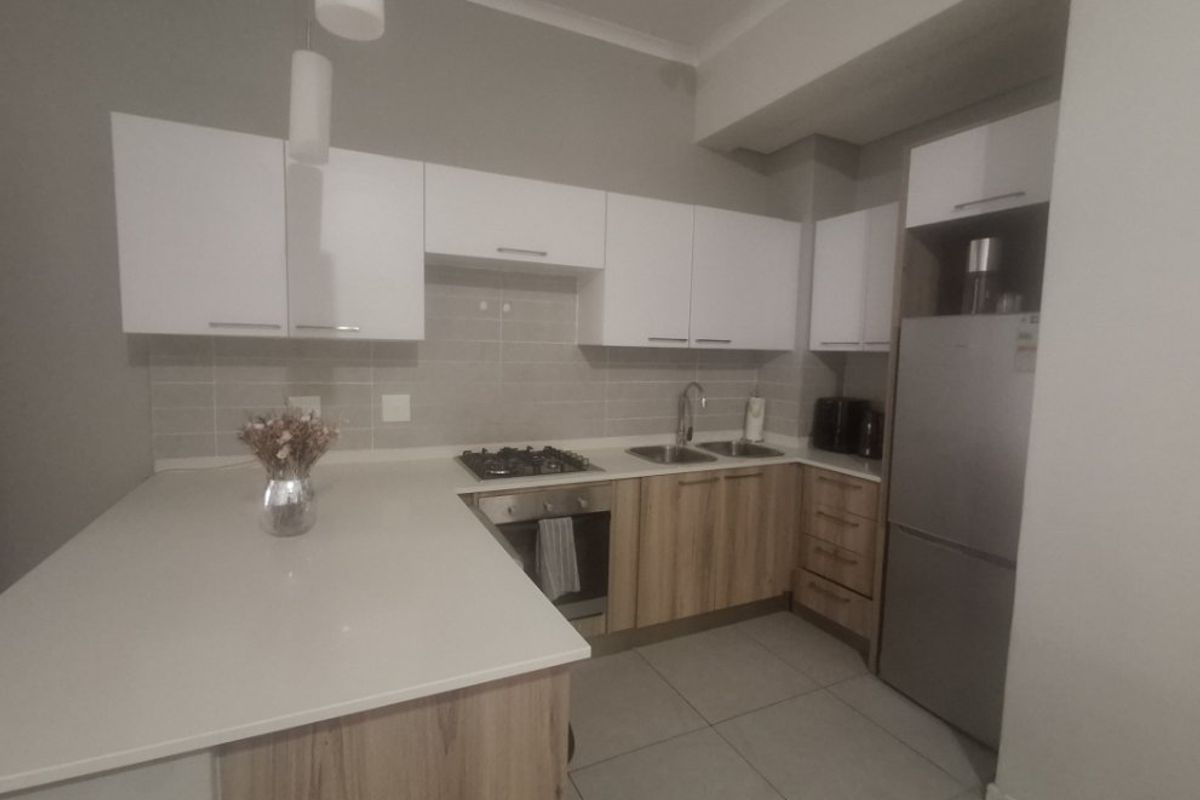Modern kitchen featuring light wood-finish cabinetry, white stone countertops, a gas hob, built-in oven, and neutral tiled backsplash.