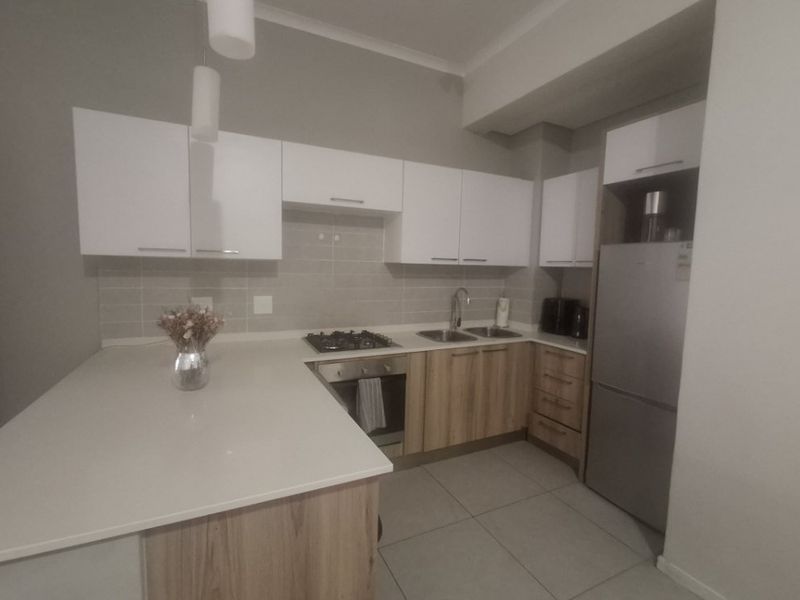 Modern kitchen featuring light wood-finish cabinetry, white stone countertops, a gas hob, built-in oven, and neutral tiled backsplash.
