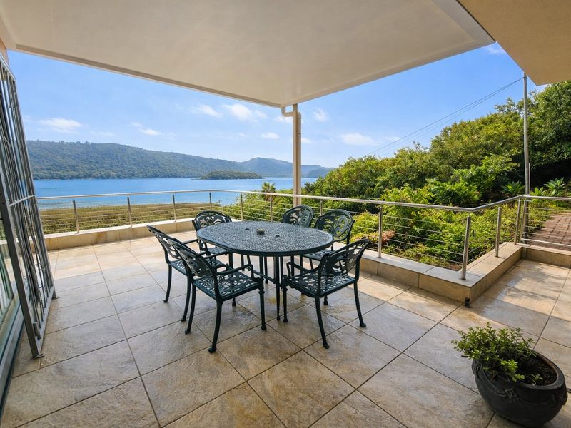 Spacious covered balcony featuring tiled flooring and stainless steel balustrades, offering expansive views of the water and surrounding landscape.