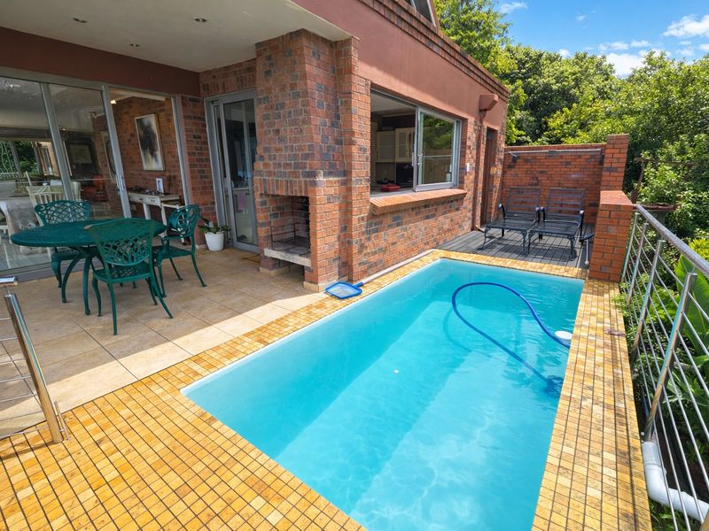 Outdoor entertainment area featuring a tiled patio, built-in brick braai, and a swimming pool with mosaic tiling, accessible via sliding glass doors.