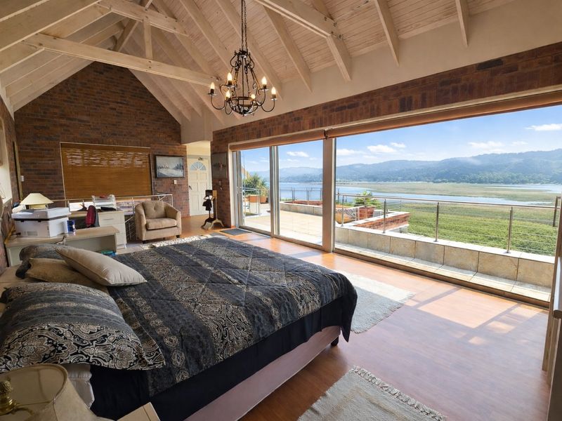 Spacious bedroom featuring vaulted timber ceilings, exposed brick walls, and large sliding doors opening onto a balcony with scenic water and mountain views.