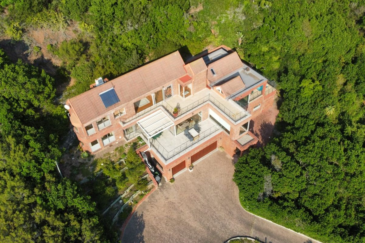 Aerial view of a multi-level brick house featuring a terracotta tile roof, solar water heating, paved driveway, and multiple balconies nestled in a wooded area.