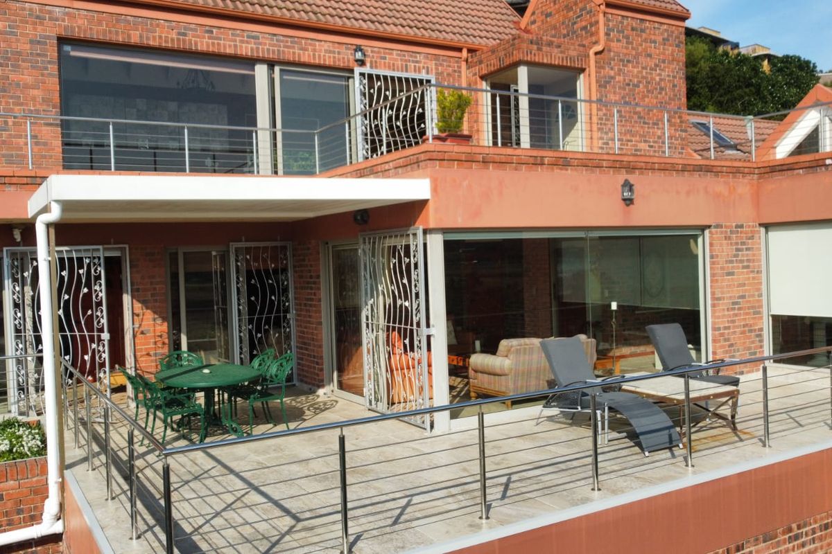 Spacious rear exterior featuring a large tiled patio with stainless steel balustrades, brick facade, and access to the interior through sliding glass doors.