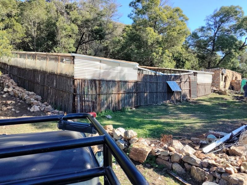 Exterior view of a farm structure featuring corrugated iron roofing, reed fencing, and a solar panel installation set against a natural landscape.