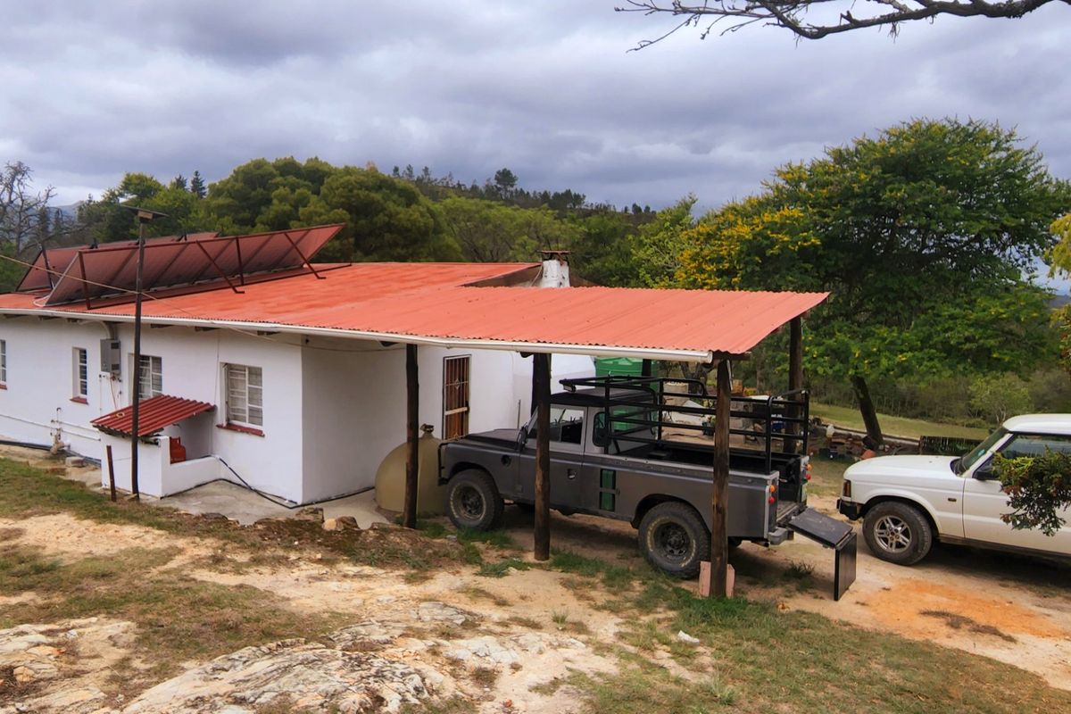 Rear view of a farm dwelling featuring a corrugated metal roof, solar water heating panels, and a covered carport area.