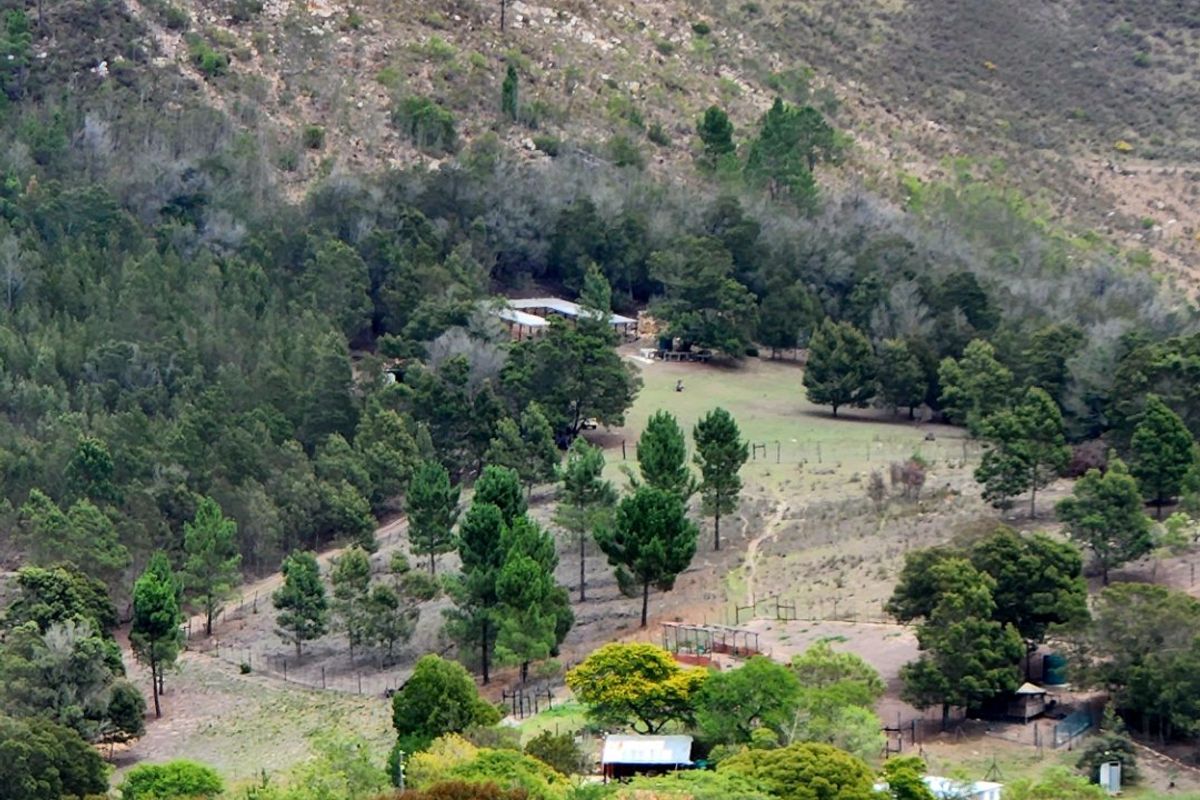 An elevated aerial view of the farm property, showcasing the surrounding landscape, forested areas, and existing outbuildings nestled within the valley.