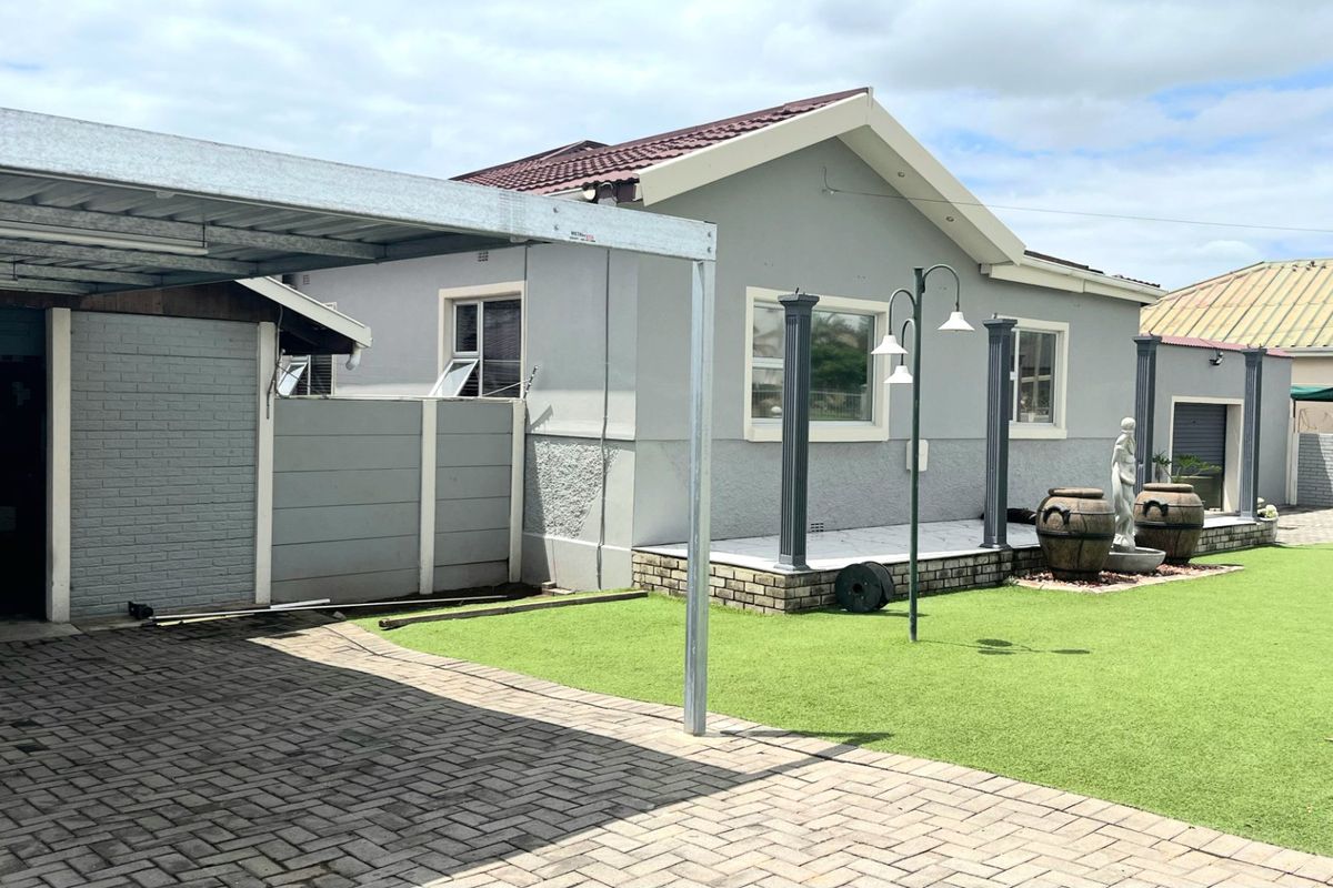 Rear exterior view featuring a paved driveway, carport, artificial lawn, and a tiled patio area with decorative pillars.