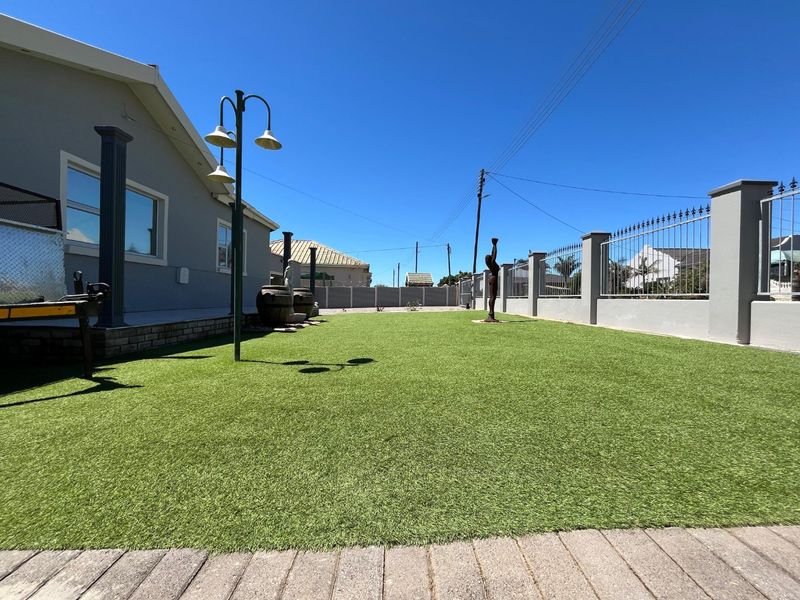 A well-maintained garden area featuring artificial turf, secure perimeter walling with metal fencing, and exterior lighting.