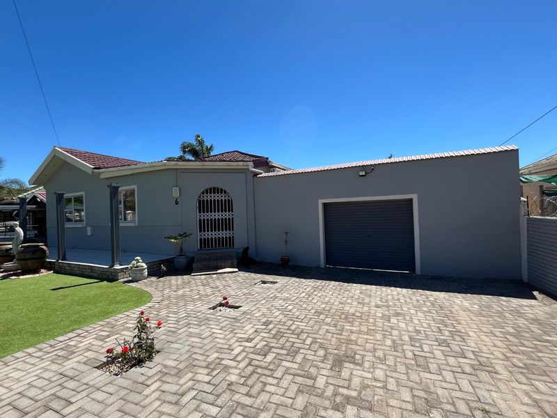 Front elevation of a well-maintained house featuring a paved driveway, single garage, covered patio area, and artificial lawn.