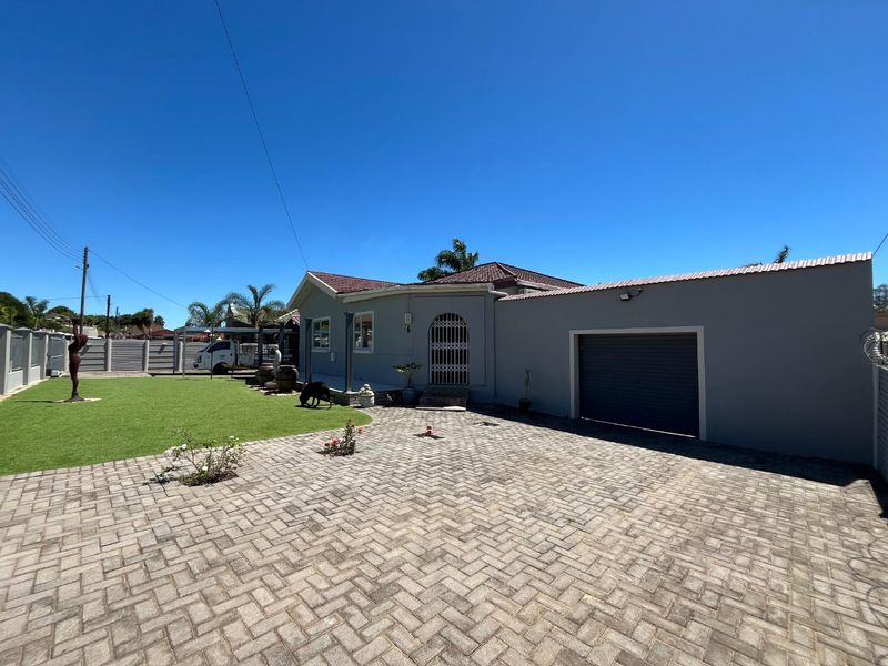 Front exterior view of the house featuring a paved driveway, artificial lawn, and an integrated garage with a secure entrance gate.