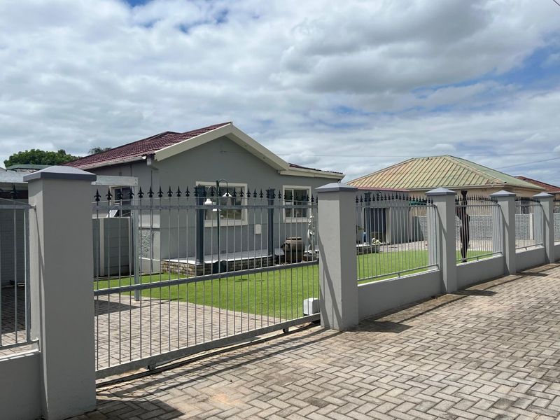 Front view of a well-maintained house featuring a secure metal perimeter fence, paved driveway, and a neat artificial lawn.
