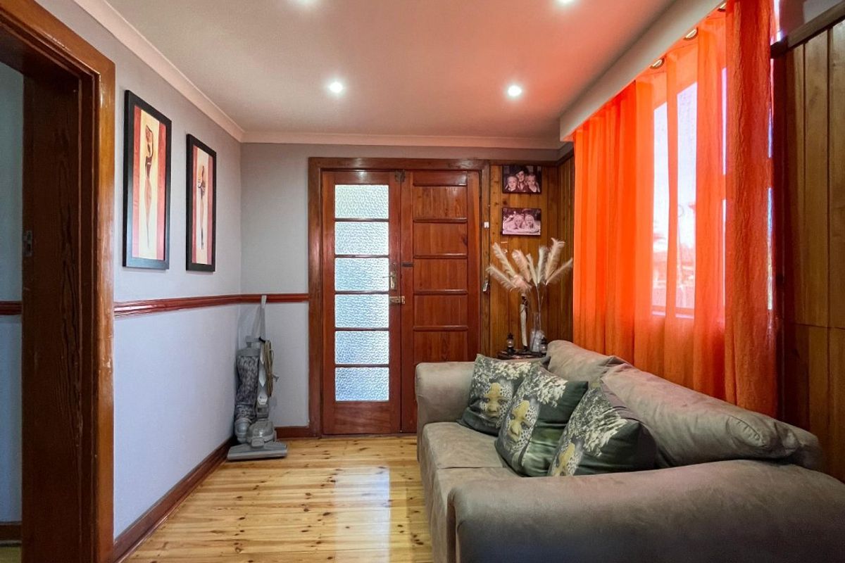 A living room featuring polished timber flooring, recessed downlighting, and classic timber door and wall paneling details.