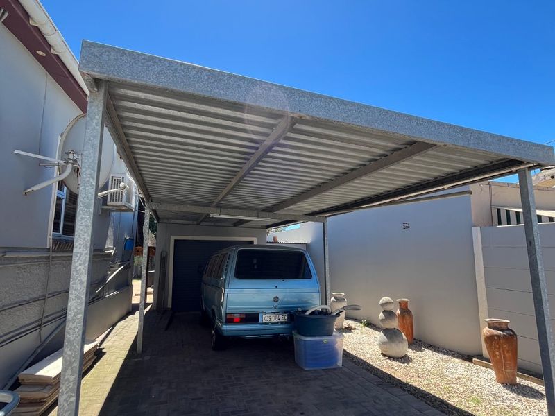 A functional rear exterior area featuring a metal carport structure over a paved driveway, adjacent to the main house wall and garage entrance.