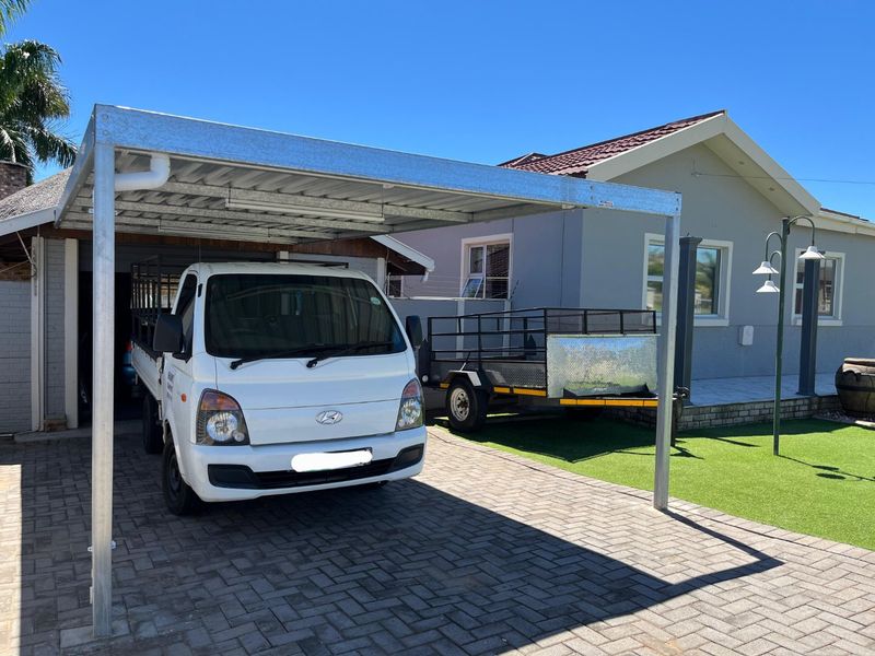 Front exterior view featuring a modern galvanized steel carport, paved driveway, and well-maintained artificial lawn area.