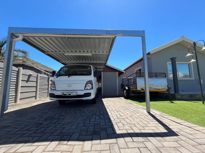 A well-maintained outdoor area featuring a modern steel carport, paved driveway, and artificial lawn, providing functional covered parking space.