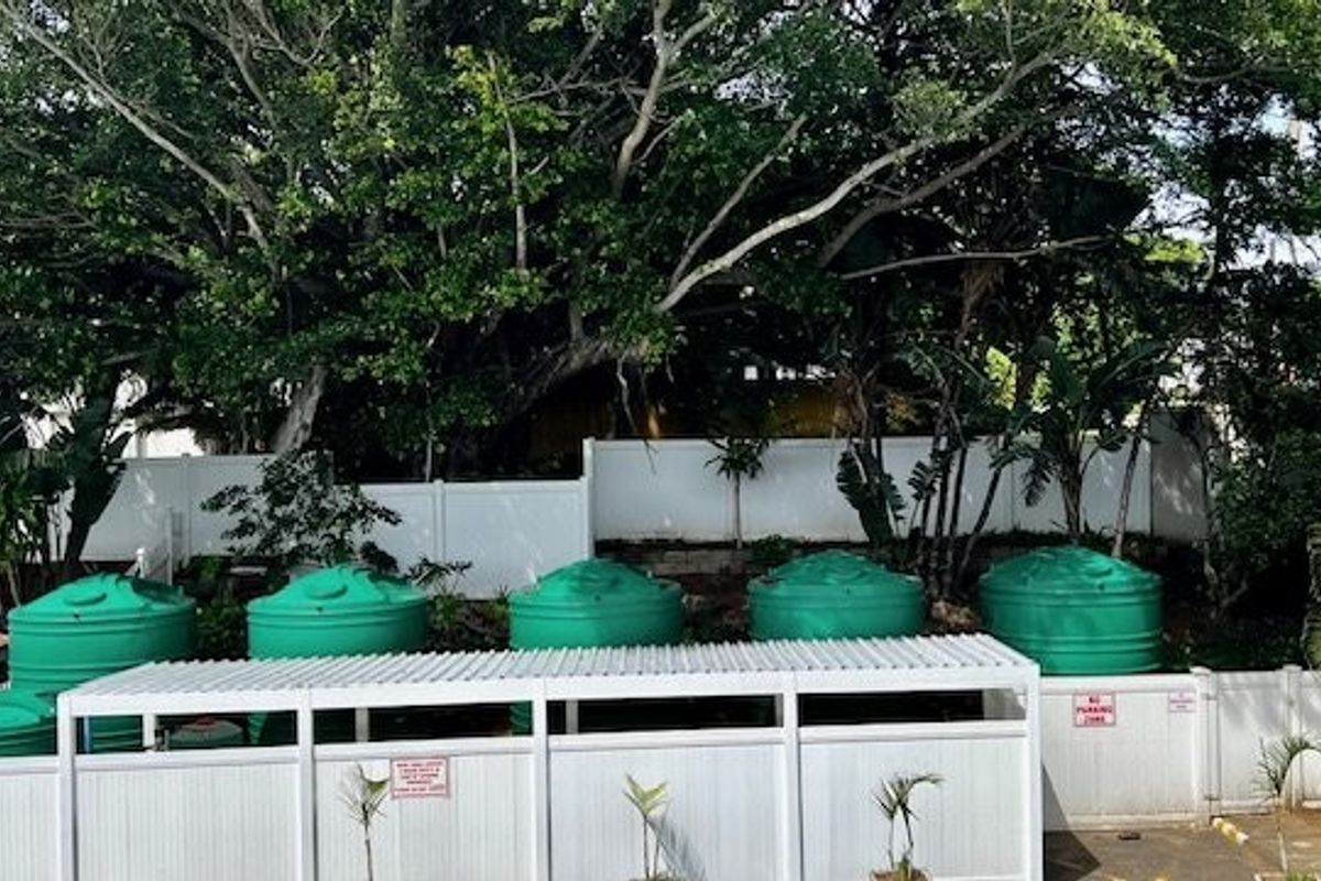 Rear exterior area featuring multiple green water storage tanks enclosed by white privacy fencing and a covered utility structure.