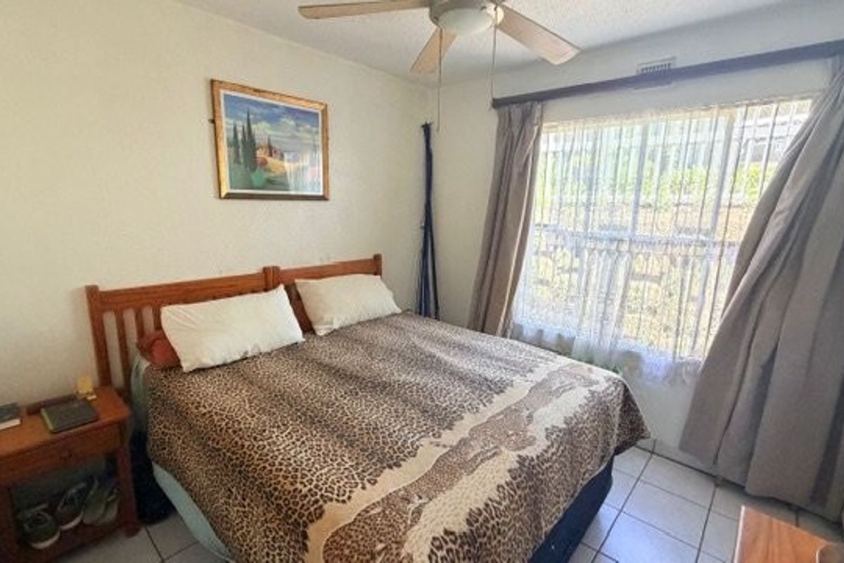 A bedroom featuring tiled flooring, a ceiling fan, and large windows with curtain tracks, offering a functional space ready for modernization.