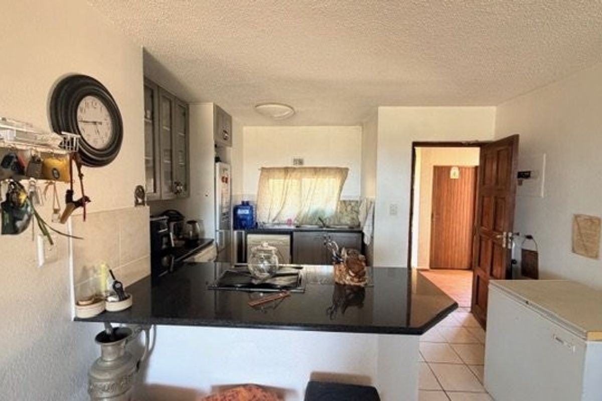 A functional kitchen featuring granite countertops, a built-in hob, and tiled flooring, offering a practical layout for daily meal preparation.