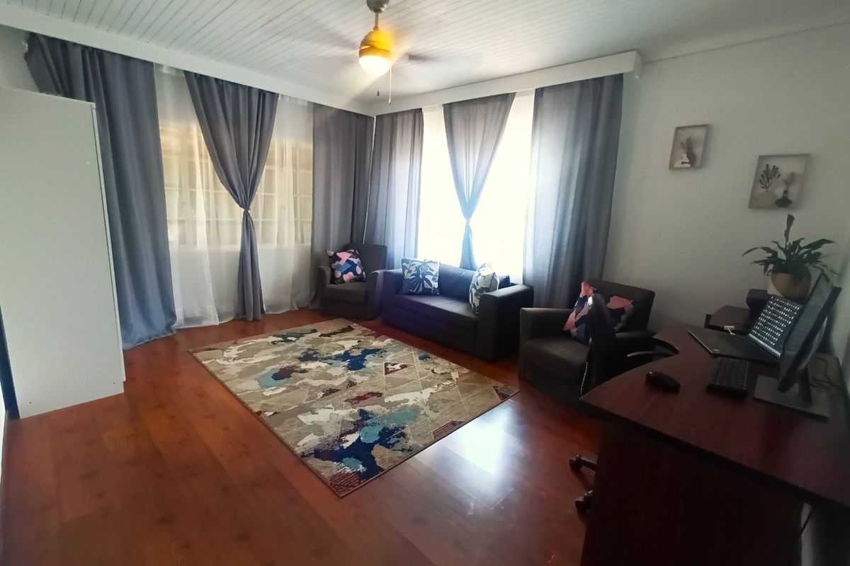 A living room featuring warm timber flooring, a tongue and groove ceiling with a central fan, and large windows allowing for natural light.