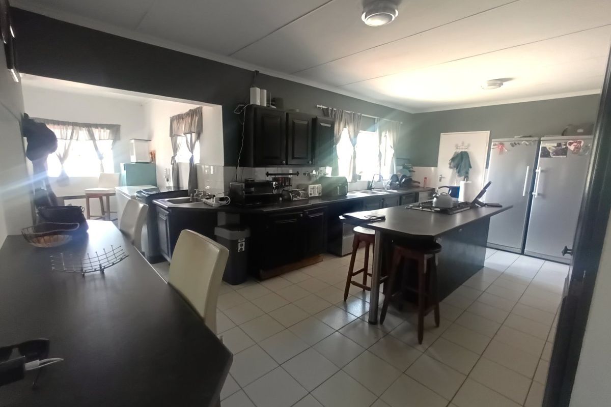 Spacious kitchen featuring dark cabinetry, a central island with a gas hob, tiled flooring, and a functional layout with an adjacent dining area.