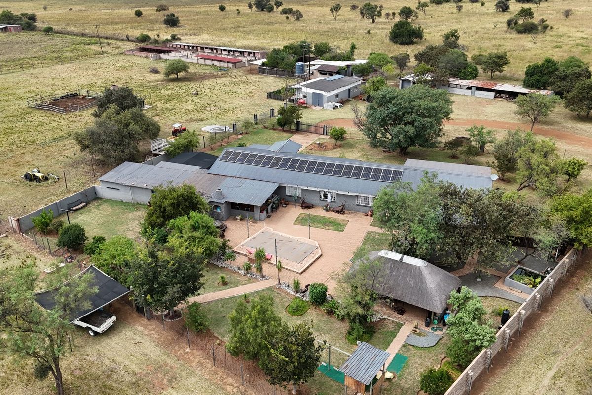 Aerial view of a farm property featuring a main residence with solar panels, a central paved courtyard, a thatched lapa, and various outbuildings.