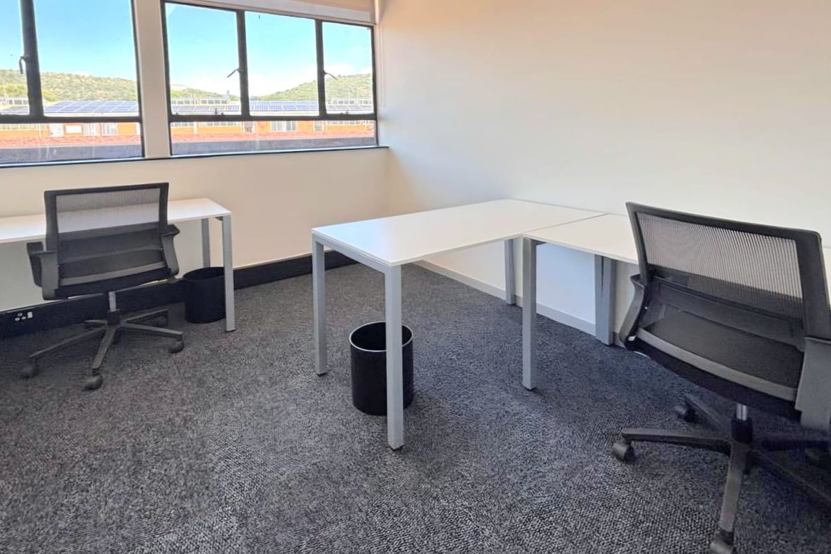 A bright, functional office space featuring large windows, neutral carpeting, and clean white walls, suitable for a professional work environment.