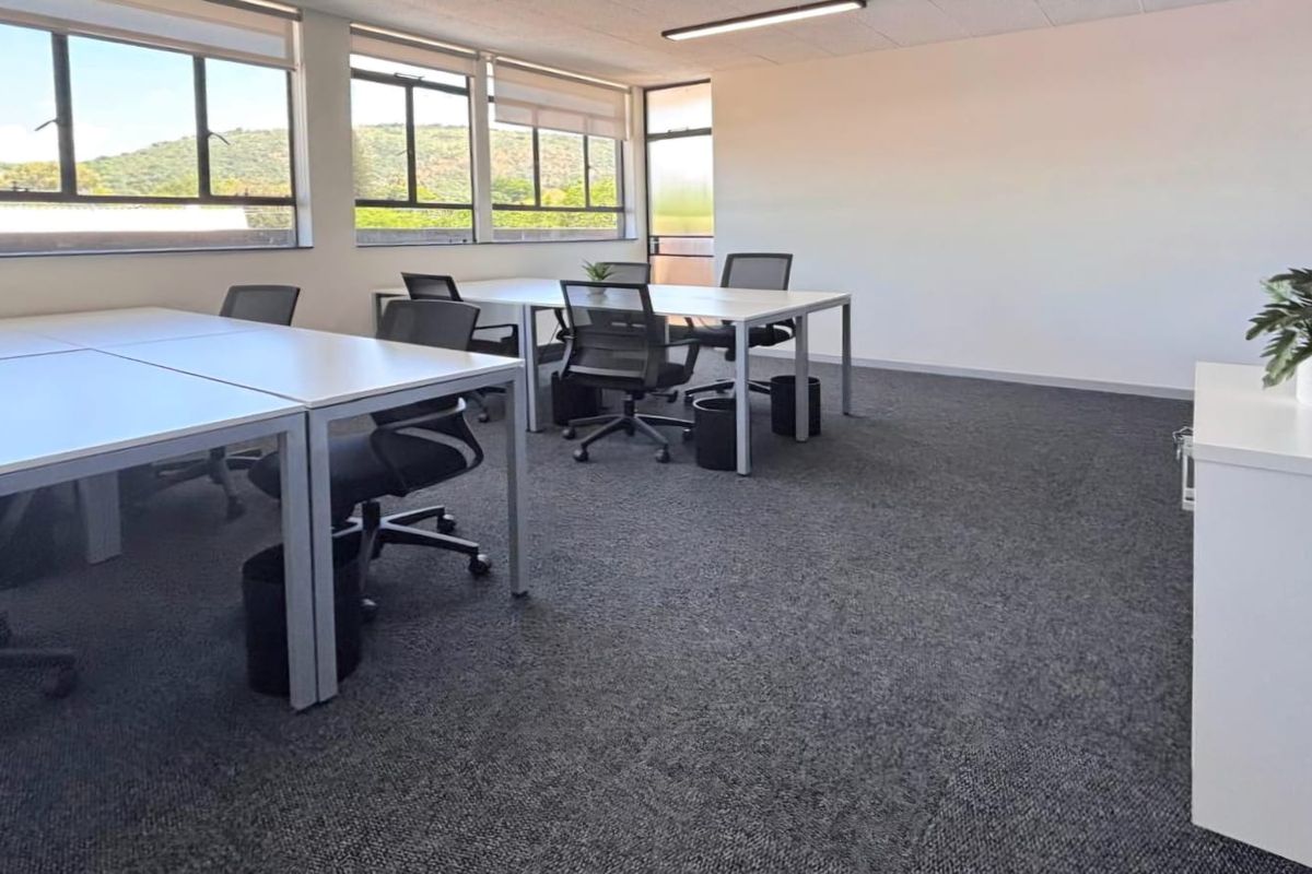 A bright, open-plan commercial office space featuring large windows, neutral carpeting, and a clean, professional layout suitable for a modern workspace.